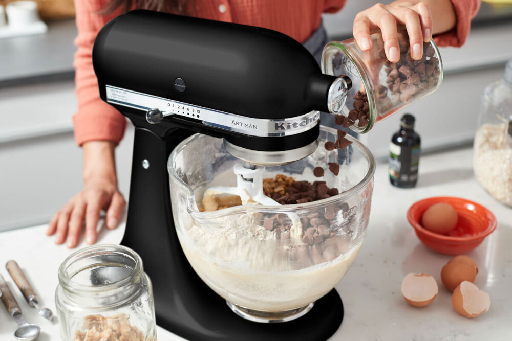 Robot kuchenny planetarny KITCHENAID Artisan 5KSM125EBM 300W czarny robot suwak na obudowie przezroczysta miska osoba dorzuca składniki do miski w każdej kuchni osłona misy z przezroczystego tworzywa sztucznego wygodne dodawanie składników praktyczne rozwiązanie proste i przyjemne przygotowywanie potraw