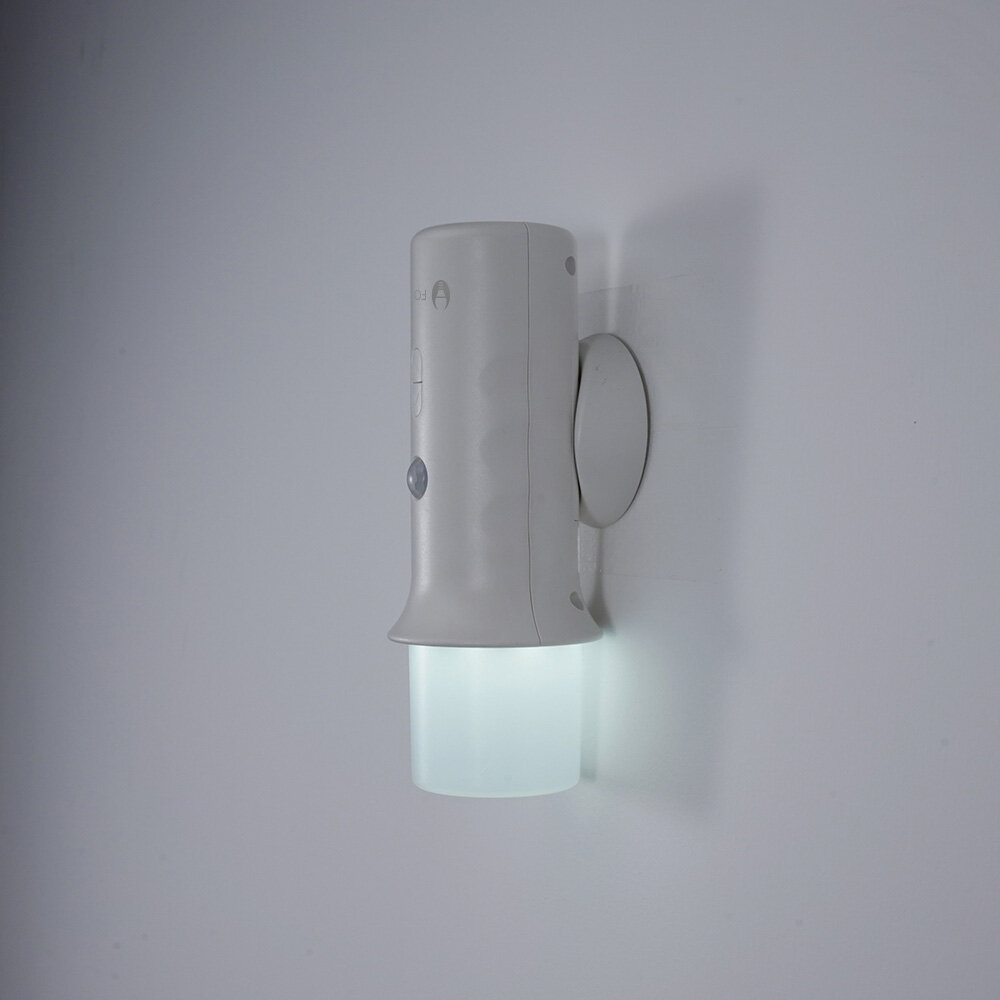 Na ścianie zamontowana jest biała lampka LED z cylindrycznym kloszem, emitująca jasne światło. Lampka posiada przycisk i czujnik ruchu na obudowie.