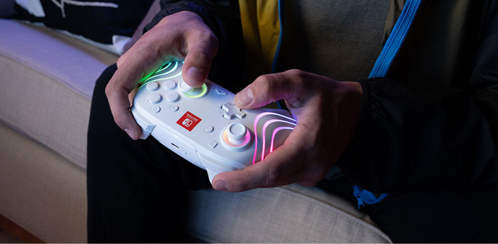 Kontroler PDP Afterglow Wave Nintendo Switch/Nintendo Switch Oled Biały prezentacja kontrolera podczas grania na nim mężczyzna siedzący na kanapie i grający akumulator 2100 mAh do 40 godzin gry bez ładowania