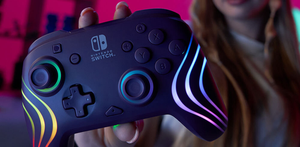 Kontroler PDP Afterglow Wave Nintendo Switch/Nintendo Switch Oled Fioletowy prezentacja kontrolera trzymanego w ręcę na różowym tle
