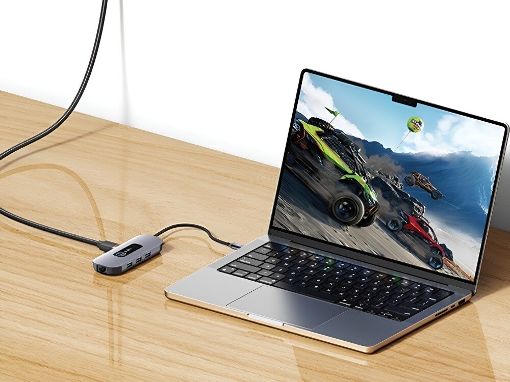 Hub USAMS SJ642HUB01 Laptop stoi na drewnianym biurku. Do portu USB-C podłączony jest hub, a na ekranie widoczna jest gra wyścigowa z samochodami terenowymi, 
            hub gadżet technologia komputer laptop