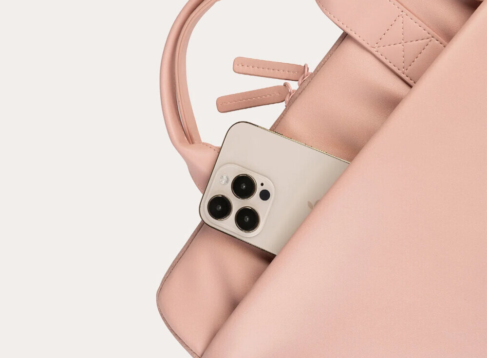 Różowa torba na laptopa z widocznym uchwytem i zamkiem błyskawicznym, z której wystaje smartfon z trzema obiektywami aparatu.