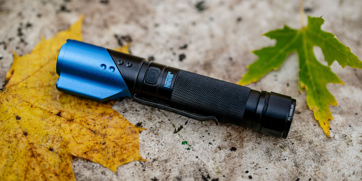 Latarka taktyczna NEWELL FL1000LUV USB-C z UV i laserem, światło, ciemność, narzędzie, warunki, Latarka Newell FL1000LUV leżąca na betonie
