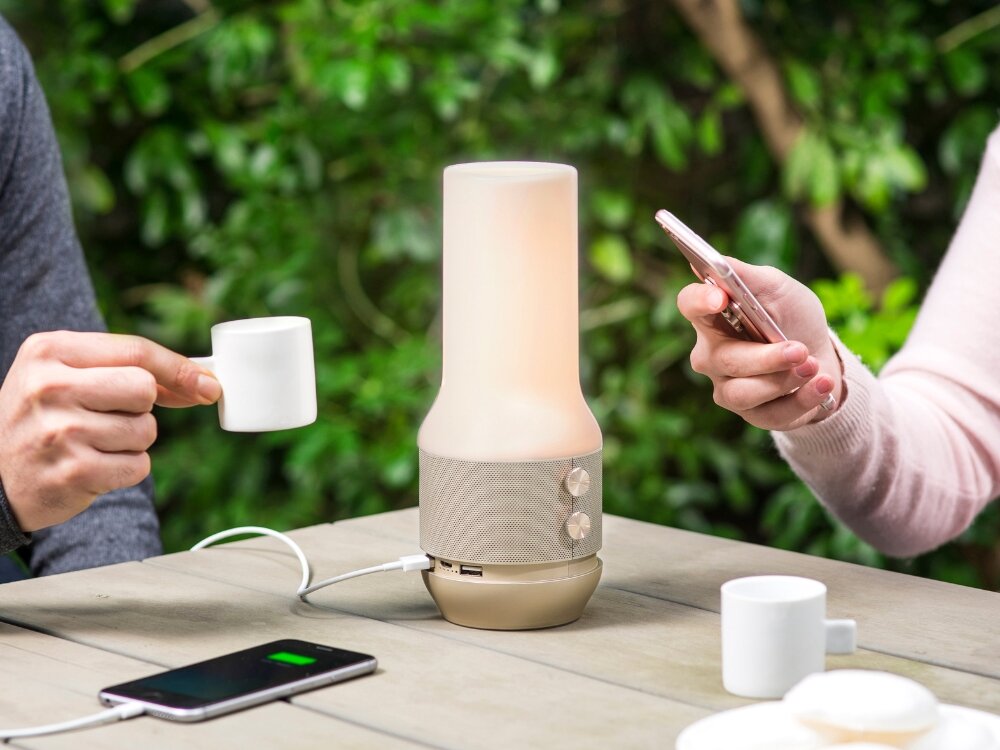 Lampka stołowa LEXON Terrace+ LA134D z głośnikiem i powerbankiem Złoty trzy funkcje jeden styl lampa złota obudowa lampa stoi na stole osoba ładuje telefon za pomocą lampy  