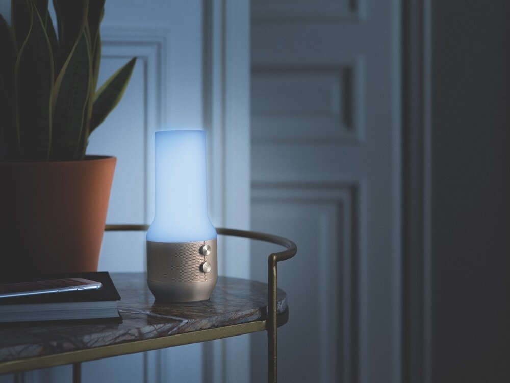 Lampka stołowa LEXON Terrace+ LA134D z głośnikiem i powerbankiem Złoty lampa z szarą podstawką stoi na stoliku przyciski unikalny akcent niepowtarzalny charakter trzystopniowa regulacja jasności możliwość zmiany barwy światła atmosfera do każdej sytuacji praca wymagająca skupienia relaksująca chwila odpoczynku minimalistyczny design funkcjonalność styl komfort na zewnątrz wyjątkowy urok 