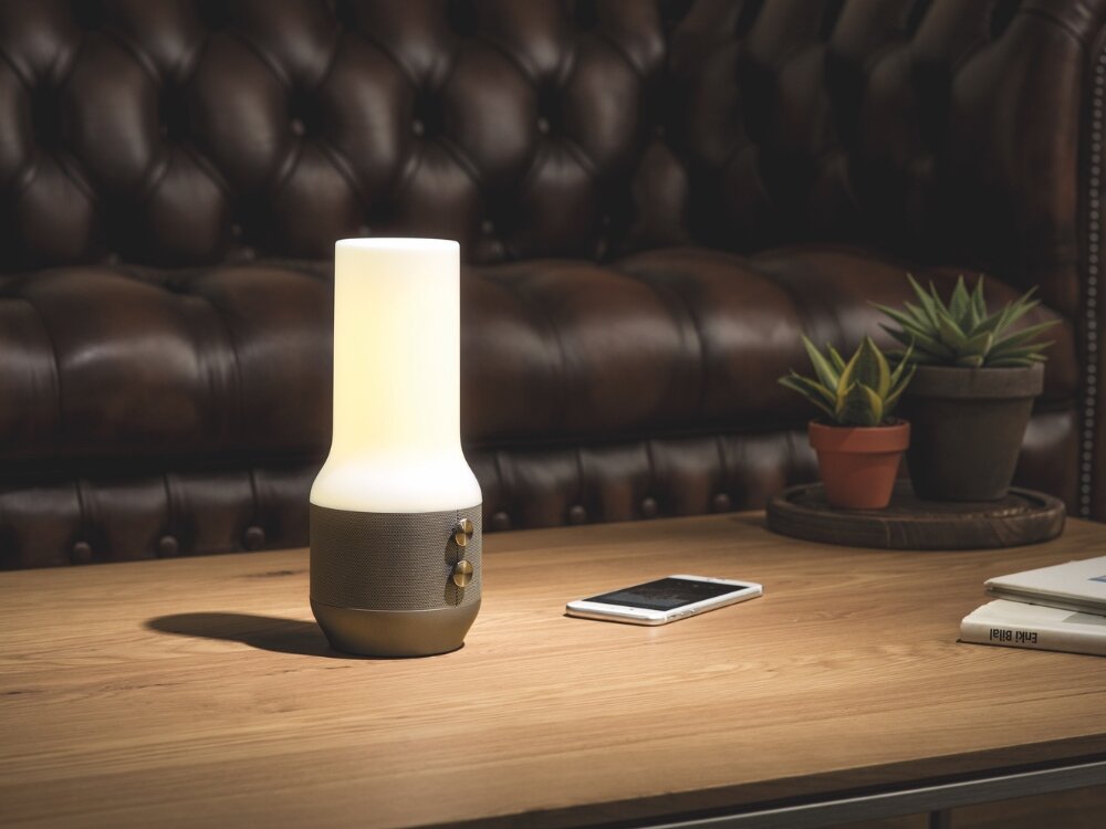 Lampka stołowa LEXON Terrace+ LA134D z głośnikiem i powerbankiem Złoty lampa z szarą podstawką stoi na stoliku przyciski obok leży telefon  funkcja stylowego oświetlenia mobilny głośnik Bluetooth wygodne bezprzewodowe odtwarzanie muzyki wyjątkowa jakość dźwięku podczas relaksujących wieczorów podczas spotkań z przyjaciółmi kompaktowe wymiary 220 x 150 mm stylowe wzornictwo różnorodne aranżacje przestrzeni 
