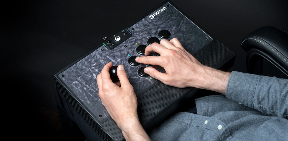 Kontroler NACON Daija Arcade Stick prezentacja kontrolera w codziennym użytkowaniu mężczyzna siedzący na fotelu i korzystający z kontrolera na ciemnym tle