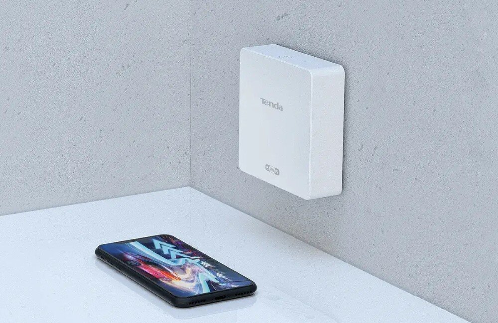 Punkt dostępu TENDA W15-Pro Urządzenie wiszące na ścianie w pobliżu leżącego na płaskiej powierzchni smartfona z kolorową grafiką na ekranie, standard Wi-Fi 6, prędkość, pasma