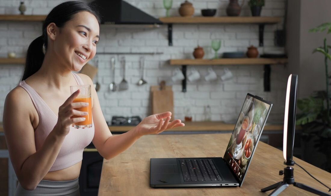 Laptop LENOVO ThinkPad Z16 G2 - Kobieta trzymająca szklankę soku, siedząca przy stole z laptopem LENOVO ThinkPad Z16 G2.