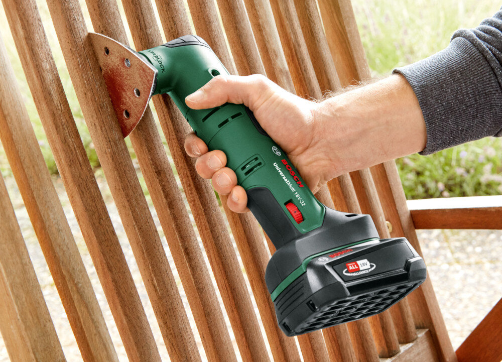 Narzędzie wielofunkcyjne BOSCH UniversalMulti 18V-32 ogród osoba trzyma narzędzie w dłoni szlifuje drewniane krzesło do różnorodnych prac związanych z majsterkowaniem i naprawami do cięcia drewna metalu tworzyw sztucznych płyt gipsowo-kartonowych usuwanie fug i zapraw zastępuje kilka narzędzi
