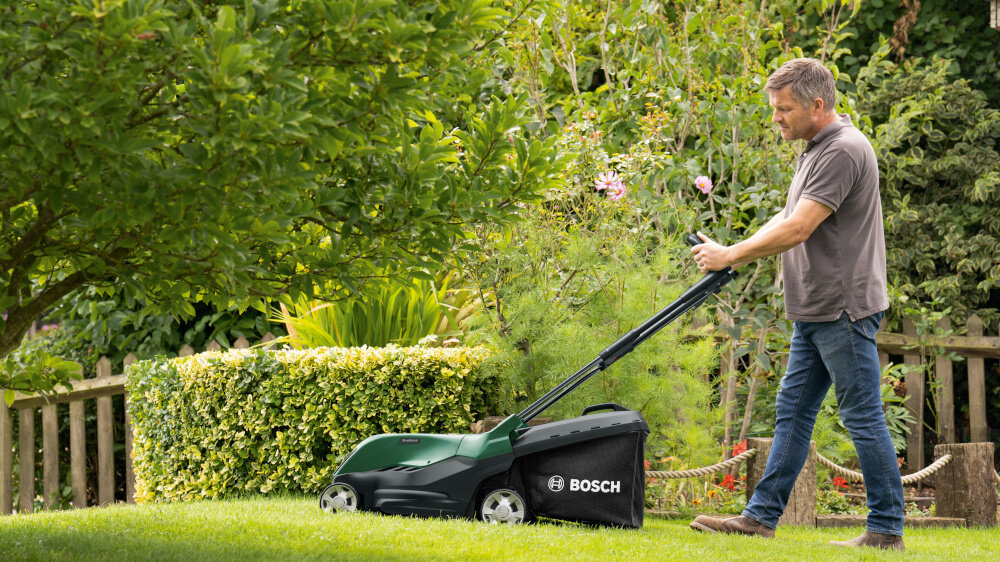 Kosiarka akumulatorowa BOSCH AdvancedlRotak 36V-44-750 06008B9G00 ogród osoba kosi trawnik w tle drzewa kwiaty krzewy zadbany trawnik piękna trawa mobilność zasilanie akumulatorowe