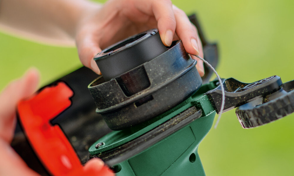 Podkaszarka akumulatorowa BOSCH UniversalGrassCut 06008C1D05 zielone tło osoba trzyma szpulę żyłki w dłoni zbliżenie na element tnący automatyczny system naciągu żyłki IntelliFEED eliminuje konieczność ręcznego dobierania długości żyłki równomierny efekt cięcia trawy przystosowana jest do żyłki tnącej o średnicy 1,6 mm szerokość robocza wynosi 260 mm