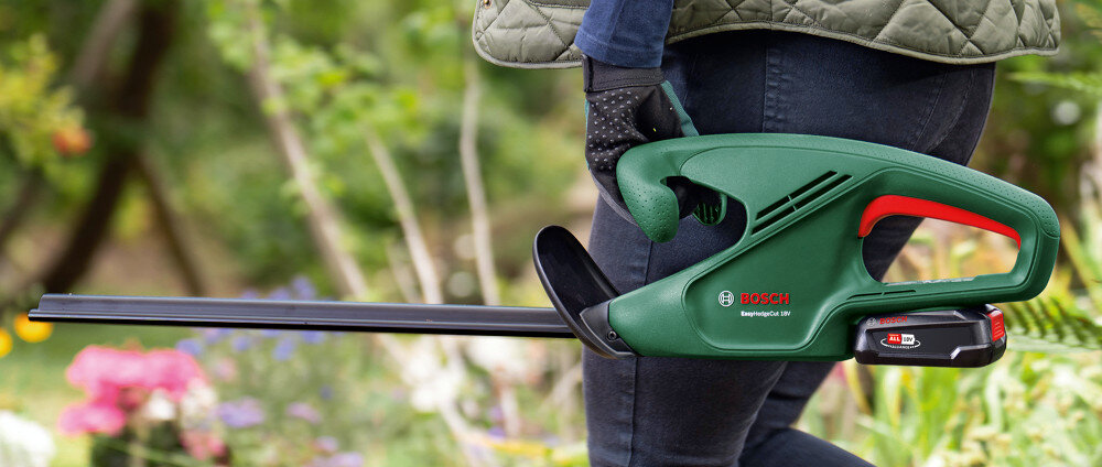 Nożyce do żywopłotu BOSCH EasyHedgeCut 18V-44-11 0600849H06 ogród osoba tnie żywopłot trzymając nożyce nad głową waga 2,3 kg bez akumulatora ergonomiczna rękojeść wygodne operowanie urządzeniem szybkie i dokładne przycinanie żywopłotu