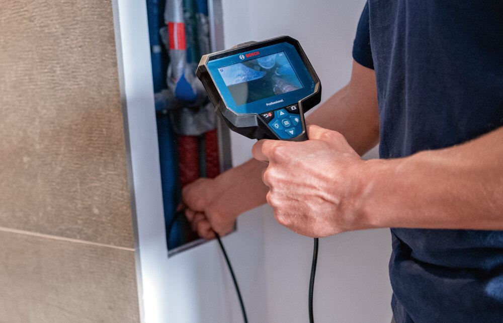 Kamera inspekcyjna BOSCH GIC 12V-5-27C 0601241401 pomieszczenie osoba sprawdza instalację w ścianie widoczne rury funkcja AutoUp automatycznie obraca obraz góra pozostaje u góry