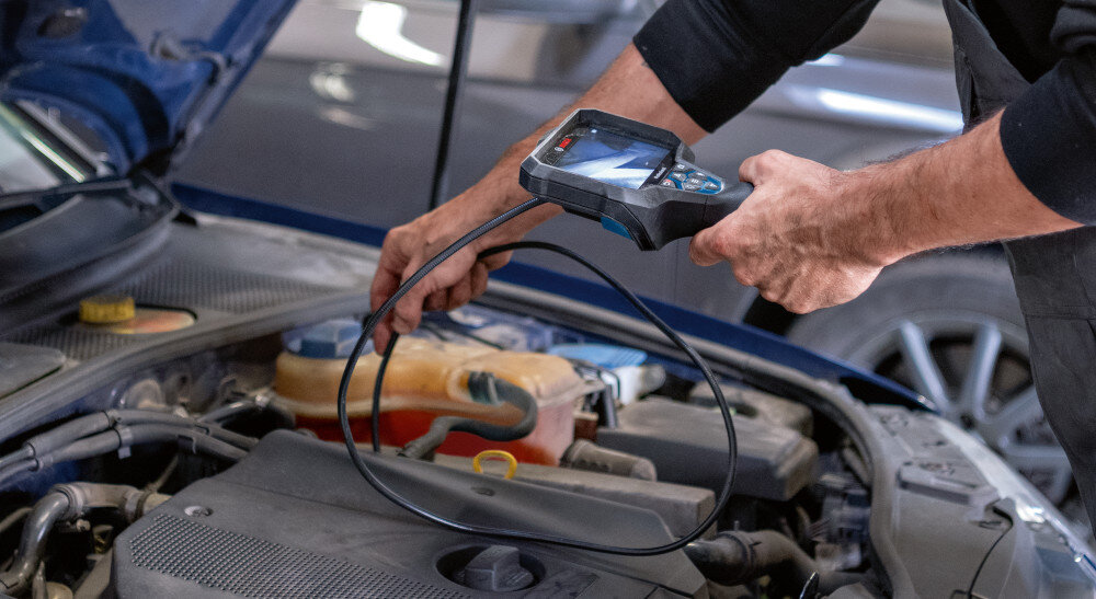 Kamera inspekcyjna BOSCH GIC 12V-5-27C 0601241401 warsztat samochodowy zbliżenie na silnik osoba wkłada przewód kamery do wnętrza auta do pracy w wymagającym środowisku dopuszczalna temperatura otoczenia podczas pracy w zakresie od -10°C do 50°C narzędzie ma klasę ochrony IP54 przewód ma klasę ochrony IP67 odporność na kurz i wodę możliwość zanurzenia przewodu do 30 minut w oleju, ropie czy słonej wodzie