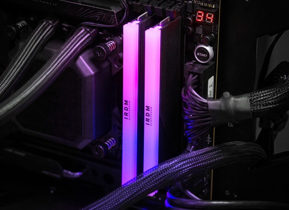 Pamięć RAM GOODRAM IRDM RGB Dwa moduły pamięci zamontowane w płycie głównej, podświetlone gradientem w kolorach różu i fioletu, otoczone czarnymi przewodami w oplocie