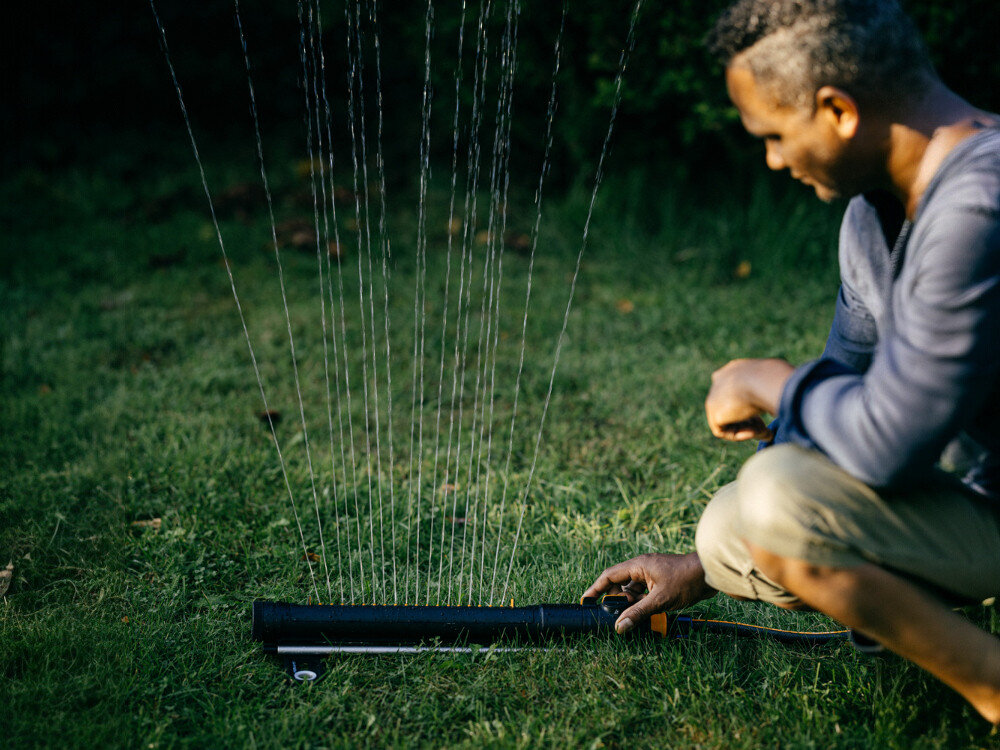 Zraszacz FISKARS 1070832, filtr, nierdzewny, czyszczenie, ochrona, mężczyzna ustawia zraszacz w ogrodzie