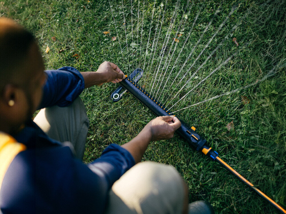 Zraszacz FISKARS 1070832, dysze, deszcz, korzenie, trawa, mężczyzna ustawia włączony zraszacz w ogrodzie
