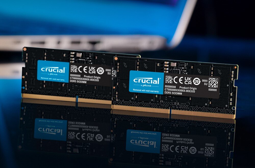 Pamięć RAM CRUCIAL 48GB (2x24GB) 5600MHz CT2K24G56C46S5 Dwa czarne moduły pamięci SODIMM stojące obok siebie na błyszczącej powierzchni, w tle widoczny laptop
