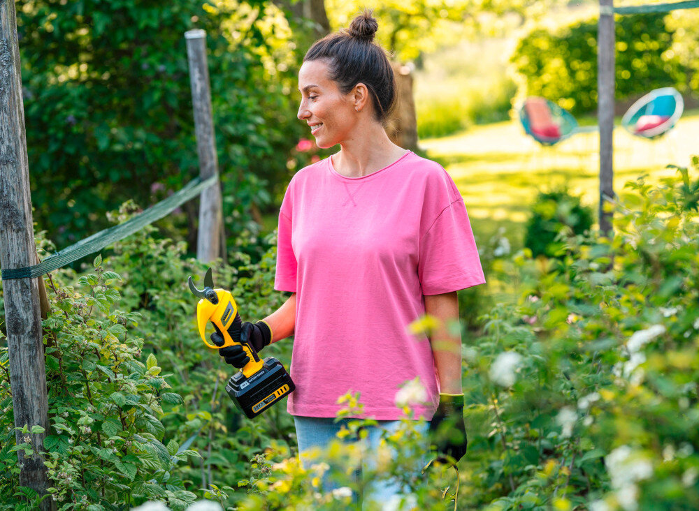 Sekator do gałęzi akumulatorowy KARCHER TLO 2-18 1.445-340.0 ogród osoba trzyma sekator w dłoni wokół rośliny waga 1,1 kg bez akumulatora ergonomiczny uchwyt odpowiednie wyważenie komfort pracy na wysokości