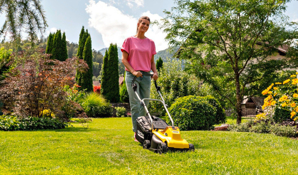 Kosiarka akumulatorowa KARCHER LMO 2-18 Battery Set 1.445-401.0 ogród trawnik osoba kosi trawnik w tle drzewa krzewy kwiaty niebo obok dom zadbany ogród efektywne koszenie mobilność