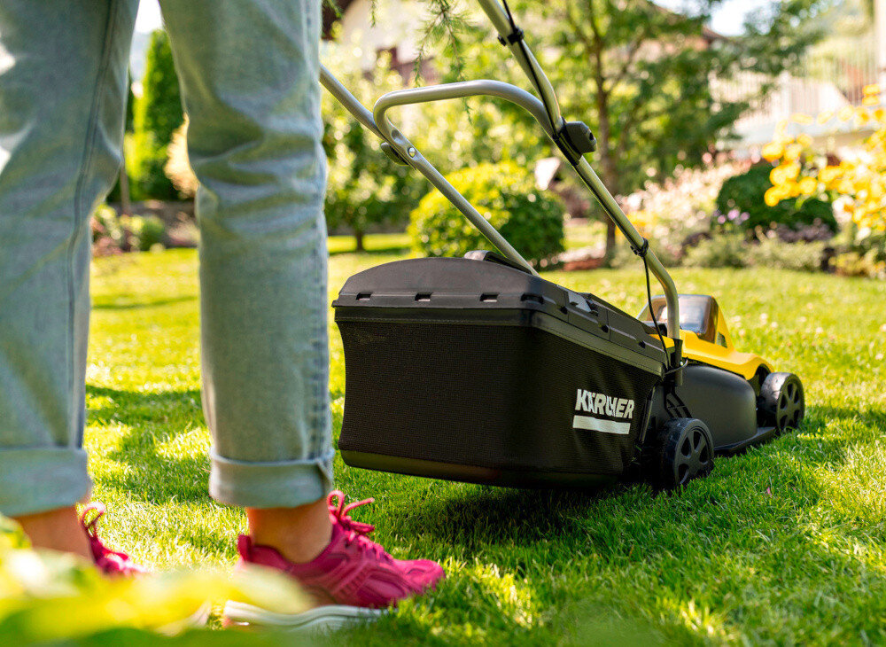 Kosiarka akumulatorowa KARCHER LMO 2-18 Battery Set 1.445-401.0 trawnik osoba kosi trawę widok od tyłu w tle drzewa kwiaty dwa praktyczne tryby pracy wyrzut tylny do kosza funkcja mulczowania trawa zbierana bezpośrednio do pojemnego kosza alternatywnie tryb mulczowania rozdrabnia źdźbła i rozprowadza je równomiernie po powierzchni trawnika