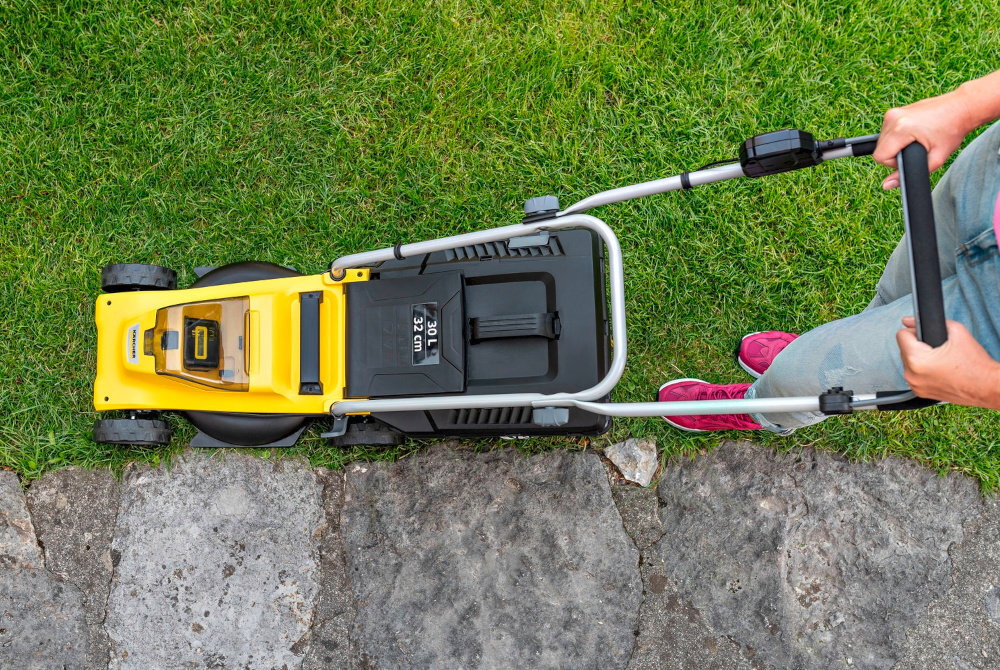 Kosiarka akumulatorowa KARCHER LMO 2-18 Battery Set 1.445-401.0 trawnik widok z góry na kosiarkę osoba kosi trawę wygoda bezpieczeństwo użytkownika grzebienie boczne automatycznie wyłapują źdźbła trawy rosnące przy krawędziach drążek sterowniczy na uchwycie prowadzącym ułatwia obsługę urządzenia klucz bezpieczeństwa chroni przed przypadkowym uruchomieniem