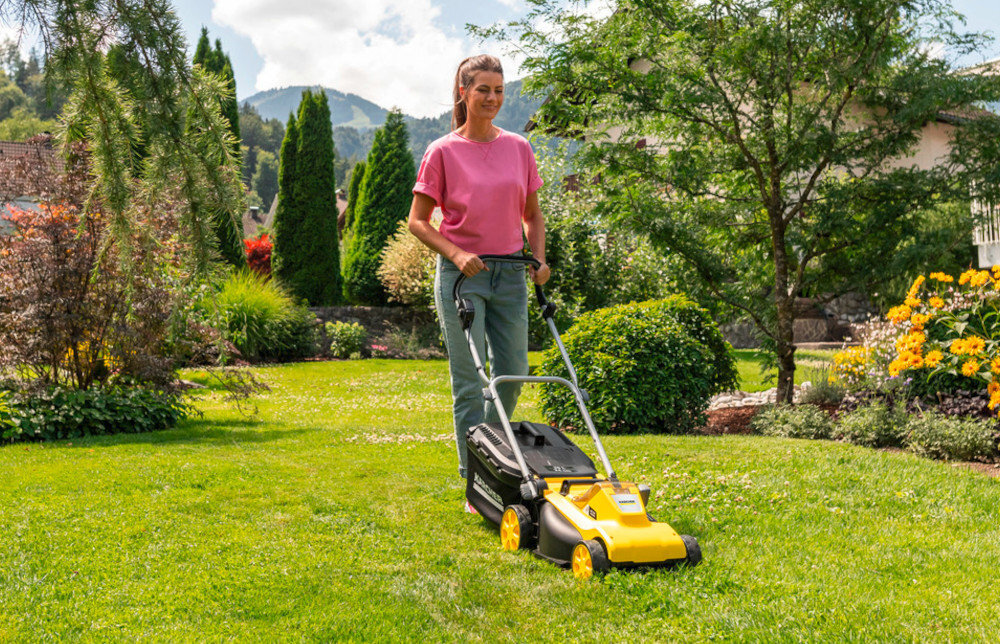 Kosiarka akumulatorowa KARCHER LMO 3-18 Battery Set 1.445-411.0 ogród trawnik osoba kosi trawnik w tle drzewa krzewy kwiaty niebo obok dom zadbany ogród efektywne koszenie mobilność