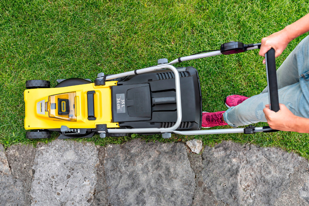 Kosiarka akumulatorowa KARCHER LMO 3-18 Battery Set 1.445-411.0 trawnik widok z góry na kosiarkę osoba kosi trawę wygoda bezpieczeństwo użytkownika grzebienie boczne automatycznie wyłapują źdźbła trawy rosnące przy krawędziach drążek sterowniczy na uchwycie prowadzącym ułatwia obsługę urządzenia klucz bezpieczeństwa chroni przed przypadkowym uruchomieniem