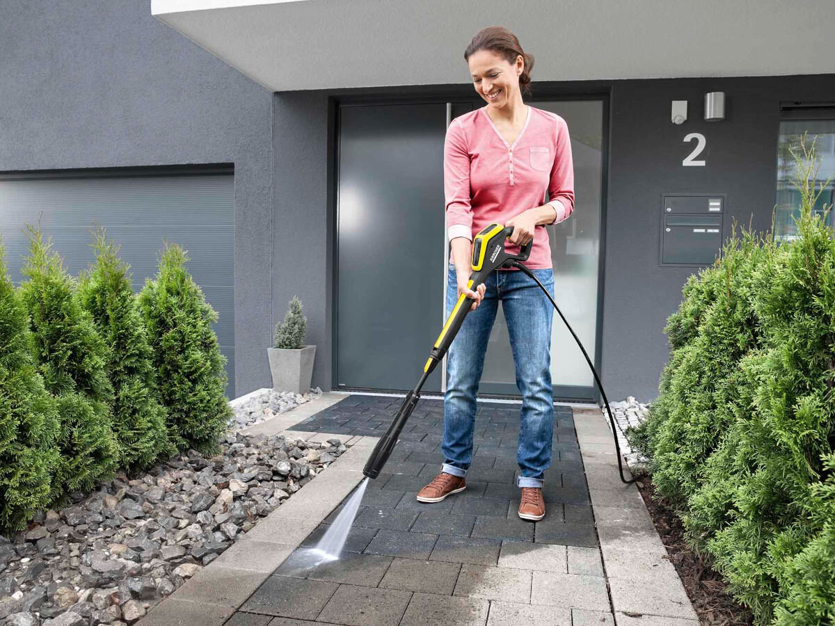 Pistolet KARCHER 2.644-327.0, tworzywo, odporność, intensywne, użytkowanie, w tle dom, kobieta przed domem czyści kostkę brukową piostoletem