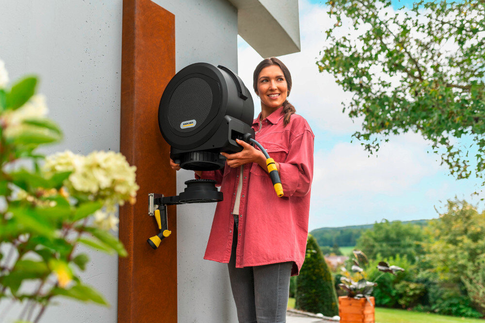 Bęben na wąż KARCHER HBX 5.35 Automatic ogród dom osoba trzyma bęben w dłoniach w tle drzewa krzewy kwiaty niebo prowadnica węża dba o równomierne wciąganie bez skręceń i supłów średnica węża 11 mm całkowita długości węża 35 m ogranicza zużycie materiału i ułatwia szybkie rozpoczęcie pracy