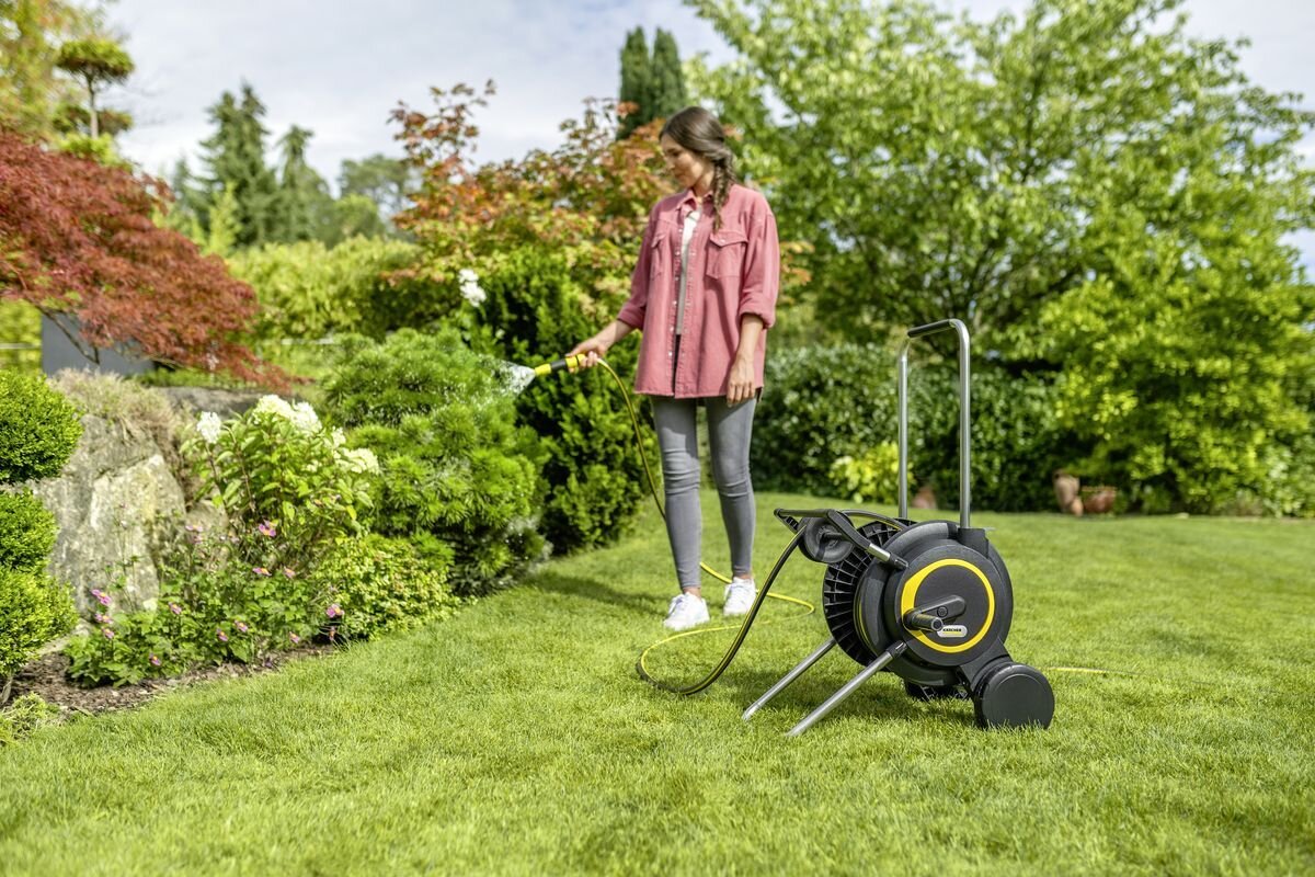 Wózek KARCHER z wężem HT 4.20 2.645-366.0, składany, uchwyt, oszczędność miejsca, przechowywanie, Kobieta podlewa krzewy w ogrodzie wężem.