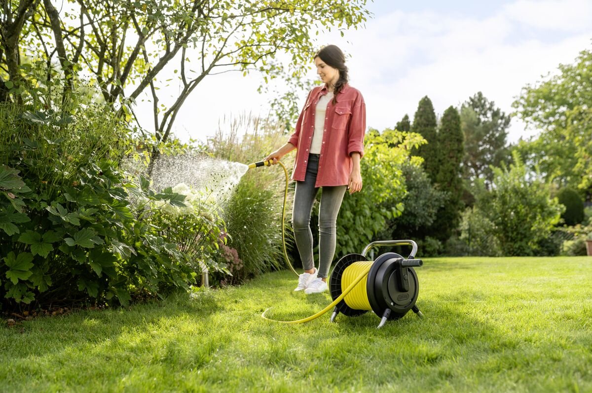 Bęben KARCHER z wężem 13 mm 1/2 10 m HR 2.10 2.645-370.0, podlewanie, rośliny, ogród, pielęgnacja, Kobieta podlewa rośliny wężem z bębna na trawie.