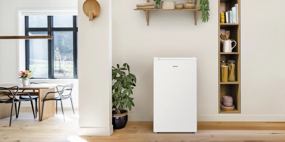 ZAMRAŻARKA GORENJE F39EPW4 Biała zamrażarka ustawiona przy ścianie w jasnym wnętrzu. Obok widoczne są roślina doniczkowa, półki z dekoracjami i stół jadalniany 61 l 3 szuflady cicha praca kompaktowa zamrażarka mechaniczne sterowanie