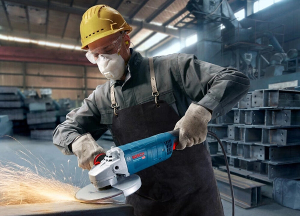 Szlifierka kątowa BOSCH GWS 27-230 J osoba trzyma szlifierkę w dłoniach szlifując metalową blachę ergonomiczna konstrukcja rękojeści wygodna obsługa ergonomiczna rączka o bardzo małym obwodzie miękka powłoka typu SoftGrip stabilny chwyt