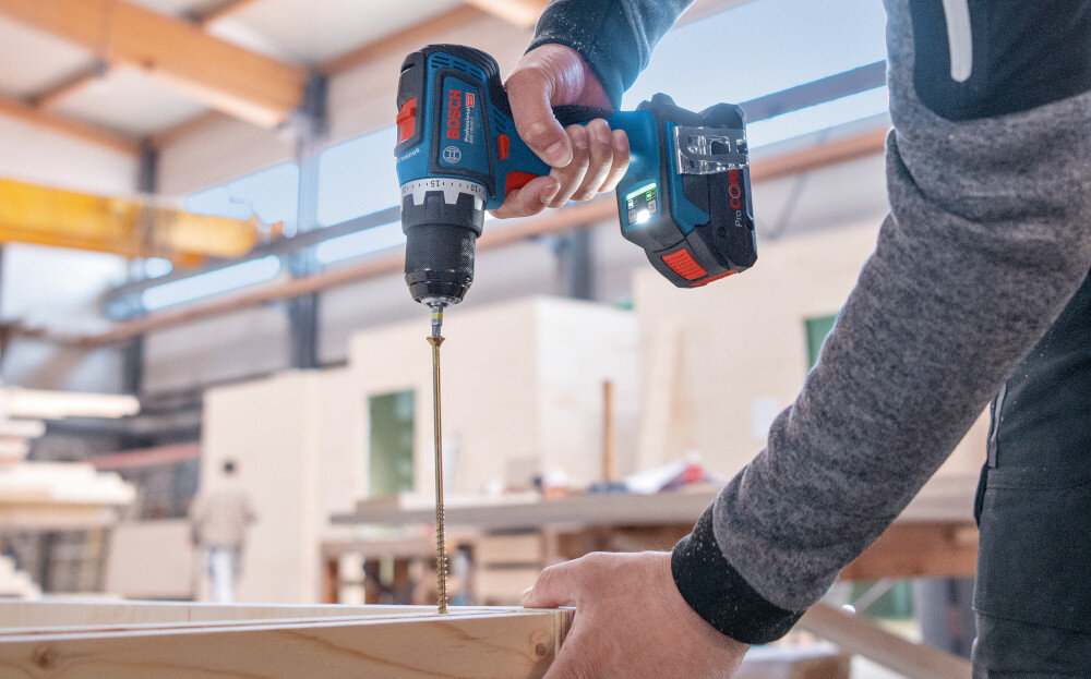 Wiertarko-wkrętarka BOSCH GSR 18V-90 FC Professional (06019K6205) pomieszczenie osoba wierci otwór w drewnianej desce rozmazane tło 21 ustawień momentu obrotowego dwa biegi obrotów precyzyjne dopasowanie siły i prędkości uniknąć przekręcania łbów śrub, zrywania gwintów czy pękania płyt powtarzalność i wysoka jakość każdego montażu większa kontrola nad efektem pracy