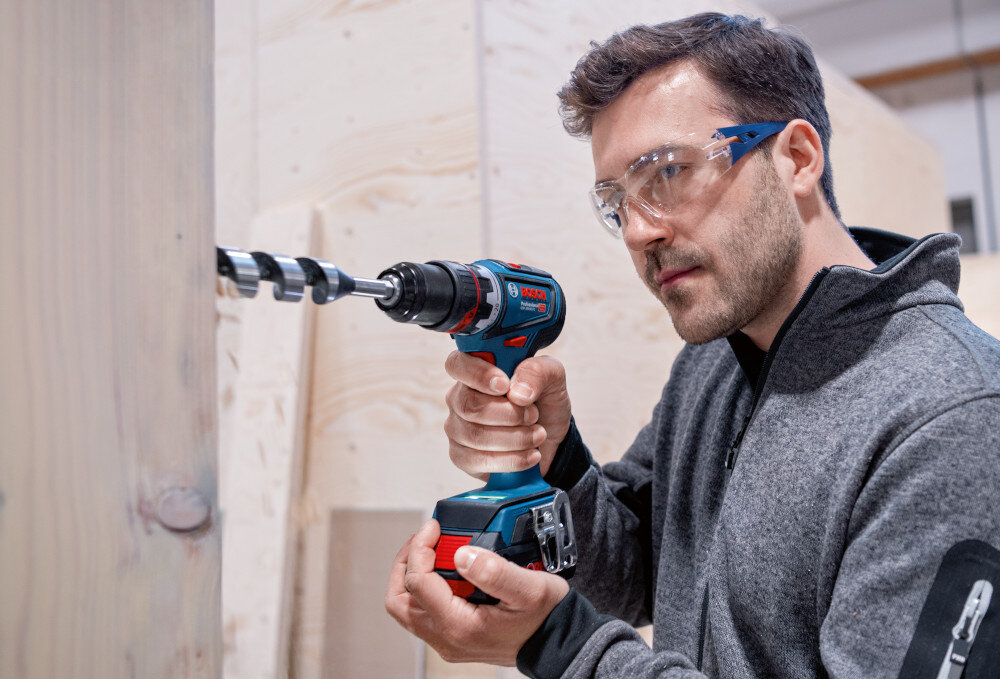 Wiertarko-wkrętarka BOSCH GSR 18V-90 FC Professional (06019K6200) pomieszczenie osoba wierci otwór w drewnianej ścianie moment obrotowy do 65 Nm prędkość do 2100 obr./min skuteczne wiercenie i wkręcanie w drewnie, metalu oraz betonie elastyczność ustawień i wszechstronność zastosowań do użytku w domu warsztacie na profesjonalnej budowie