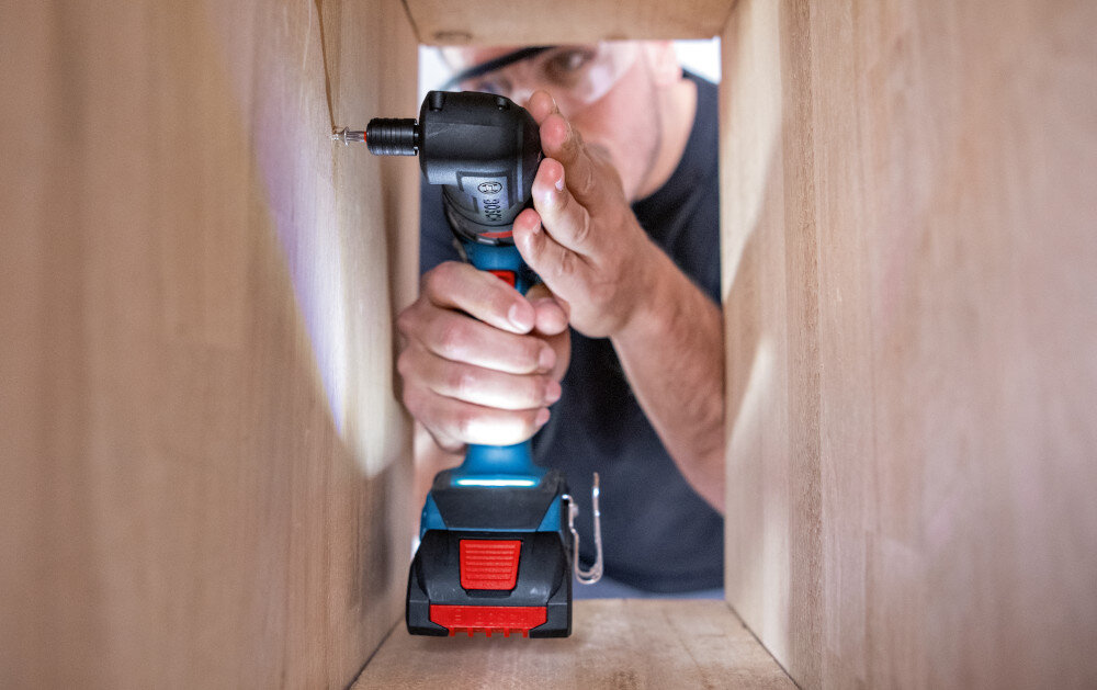 Wiertarko-wkrętarka BOSCH GSR 18V-90 FC Professional (06019K6202) pomieszczenie osoba przykręca śrubkę w drewnianej szafce silnik bezszczotkowy ogranicza straty energii i nagrzewanie rzadsze przerwy serwisowe i stabilną moc system EMP chroni napęd przed przeciążeniem długa żywotność i stabilna wydajność