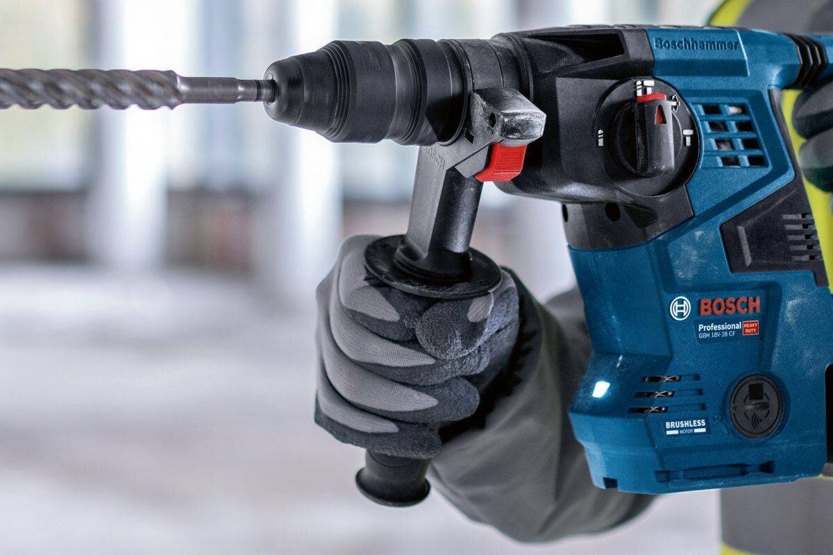 BOSCH GBH 18V-28 C 3,3 kg bez akumulatora ergonomiczny uchwyt cięższymi młotami antypoślizgowa powierzchnia rękojeści - Zbliżenie na dłonie w rękawicach ochronnych trzymające młot udarowo-obrotowy podczas pracy.