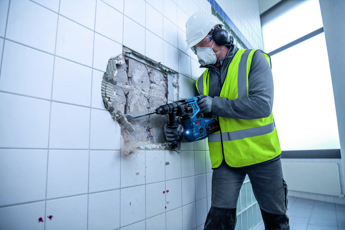 BOSCH GBH 18V-28 C Funkcja udaru nominalnej energii udaru 1,5 J liczbie udarów do 5000 obr/min Prędkość obrotowa bez obciążenia wynosi 0–900 obr/min - Mężczyzna w okularach ochronnych trzyma oburącz pracujący młot udarowo-obrotowegy.