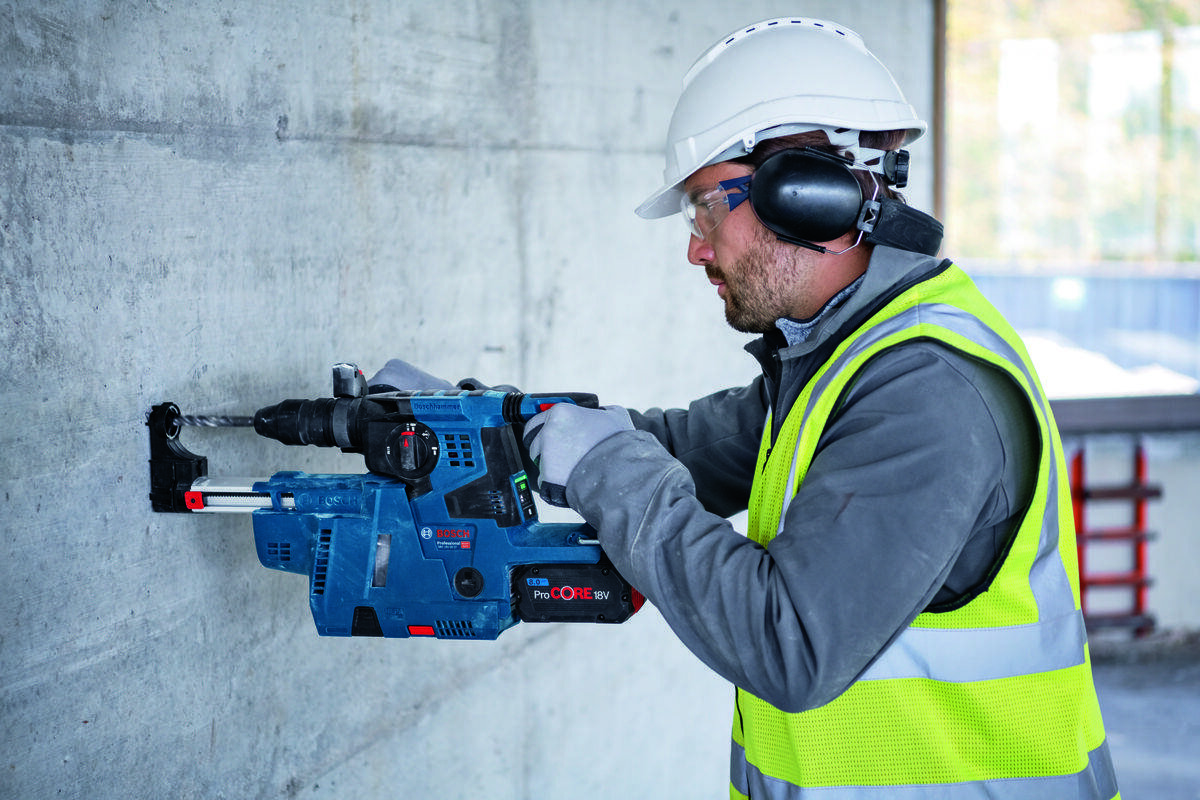 BOSCH GBH 18V-28 C BOSCH GBH 18V-28 C GDE 18V-16 Professional bezpyłową pracę młotami bez odsysania pyłu - Mężczyzna w okularach ochronnych obsługuje urządzenie przy ścianie z odsysaczem pyłu.