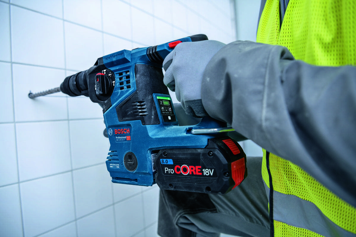 BOSCH GBH 18V-28 C obsługuje wiertła SDS plus 4–28 mm 8–18 mm wiertarkami uniwersalnymi twardymi materiałami - Mężczyzna wierci otwór w ścianie używając młota udarowo-obrotowego