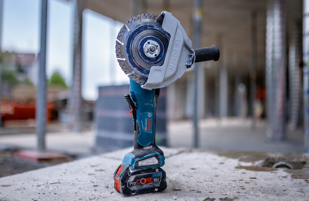 Szlifierka kątowa BOSCH Professional GWS 18V-180 P solo 0 601 9H6 L01 szlifierka stoi na akumulatorze na betonowej powierzchni w tle budynek wszechstronne narzędzie dla majsterkowiczów bezpieczne użytkowanie kontrola potężne obroty