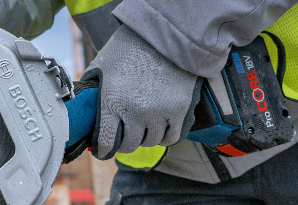 Szlifierka kątowa BOSCH Professional GWS 18V-180 P solo 0 601 9H6 L01 zbliżenie na rękojeść osoba trzyma szlifierkę w dłoni ergonomiczna konstrukcja rękojeści niska waga 2,8 kg wygodna obsługa ergonomiczna rączka o bardzo małym obwodzie powłoka typu SoftGrip