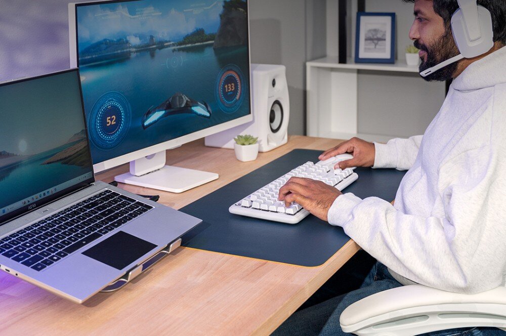 Pamięć RAM CRUCIAL 32GB (2x16GB) 5600MHz CT2K16G56C46S5 Osoba siedząca przy biurku grająca na komputerze z dwoma ekranami, z laptopem po lewej stronie i klawiaturą z białymi klawiszami