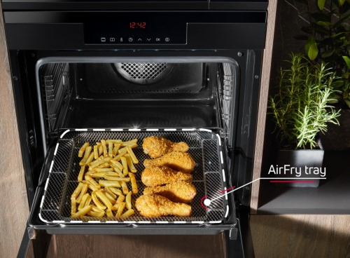 Wysunięta blacha piekarnika z frytkami i kurczakiem w panierce 