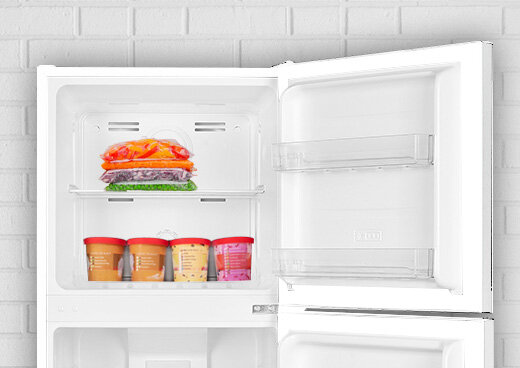 Zbliżenie na zamrażalnik górny lodówki MPM-125-CZ-08/E. Znajdują się w nim warzywa i lody.