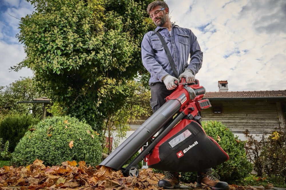 Dmuchawa do liści akumulatorowa EINHELL Venturro 36-240 3433640 ogród trawnik drzewa niebo osoba zdmuchuje liście z ziemi pasek na ramię koła prowadzące pasek odciąża ręce i kręgosłup koła ułatwiają prowadzenie urządzenia po podłożu waga 3,55 kg poręczna i dobrze wyważona