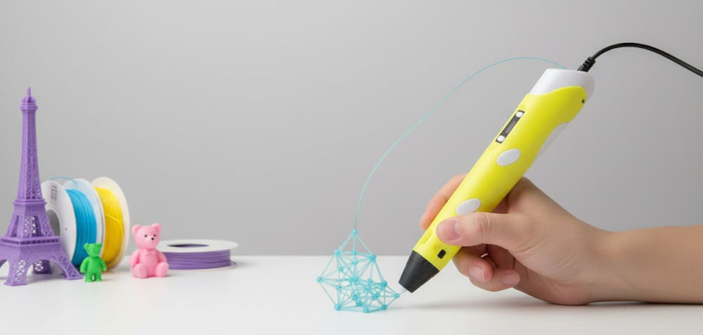 Długopis 3D EXTRALINK Smart Life ABS / PLA, Średnica dyszy 1.75 mm Żółty prezentacja długopisu podczas użytkowania na białym blacie wydrukowane już modele