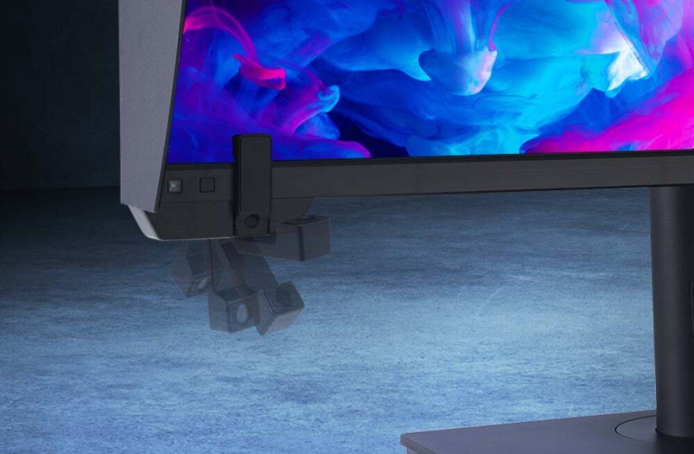 Monitor ASUS ProArt PA32UCXR Zbliżenie na dolny róg monitora z ruchomym, wysuwanym kolorymetrem. W tle rozmazane, niebiesko-różowe światło, kalibracja, oprogramowanie, profile kolorystyczne